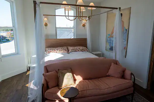 Elegant bedroom with a canopy bed and pink sofa under natural light.